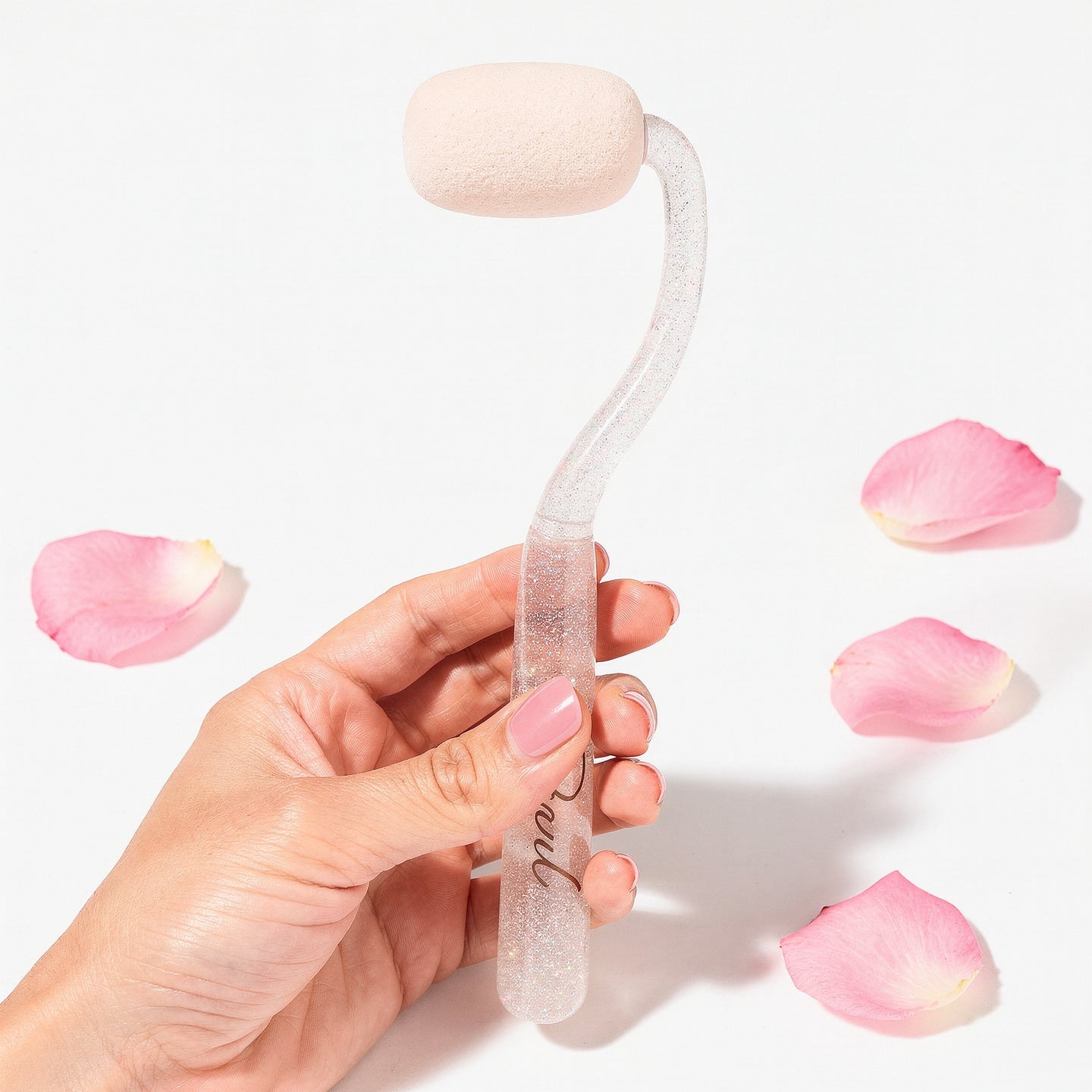 Hand holding a clear silicone tool with pink accents, surrounded by pink petals on a light background